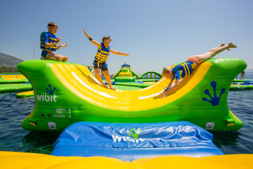 children play on the inflatable half pipe feature on the floating playground on the lake