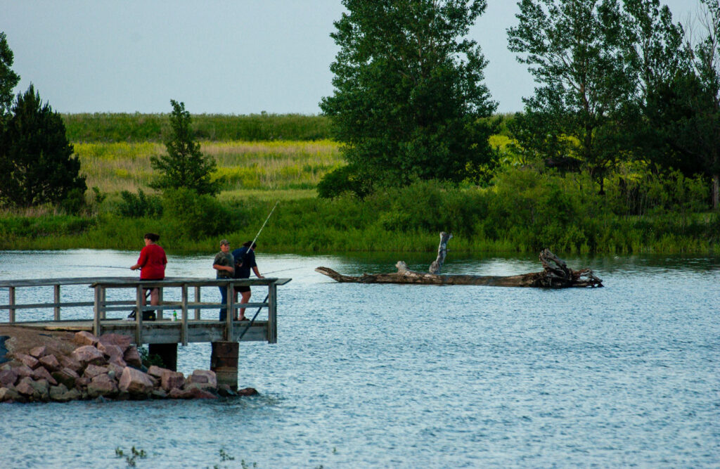 three people fishing from a fishing pier on a lake