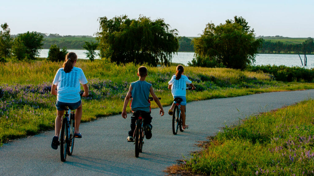 Three youth ride their bikes on a trail near a lake