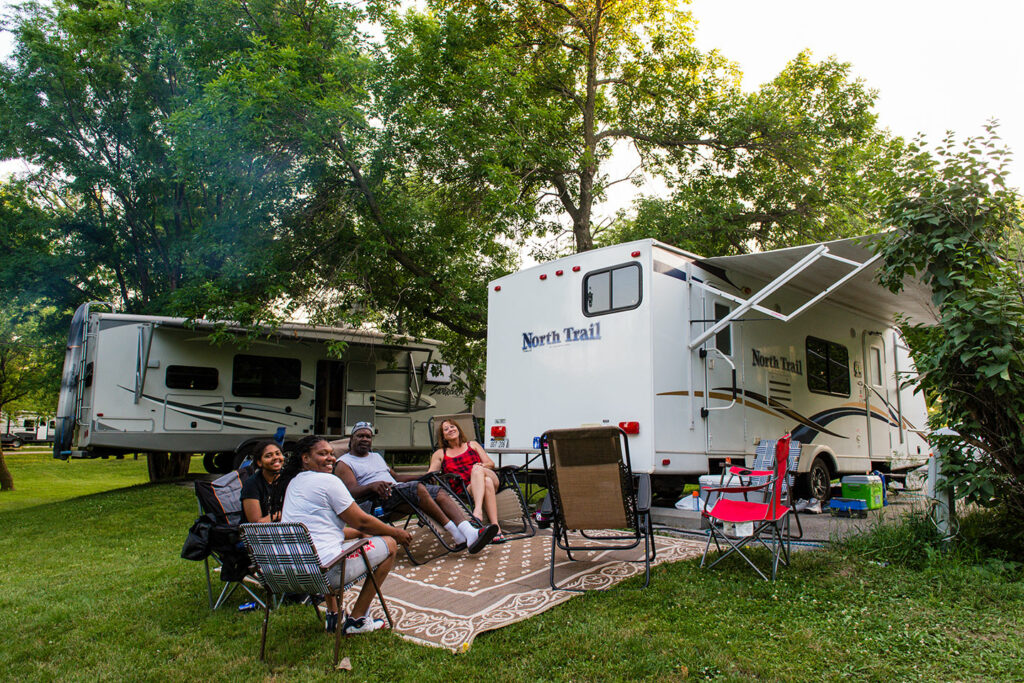 A smiling family camps with their RV in a shady campsite