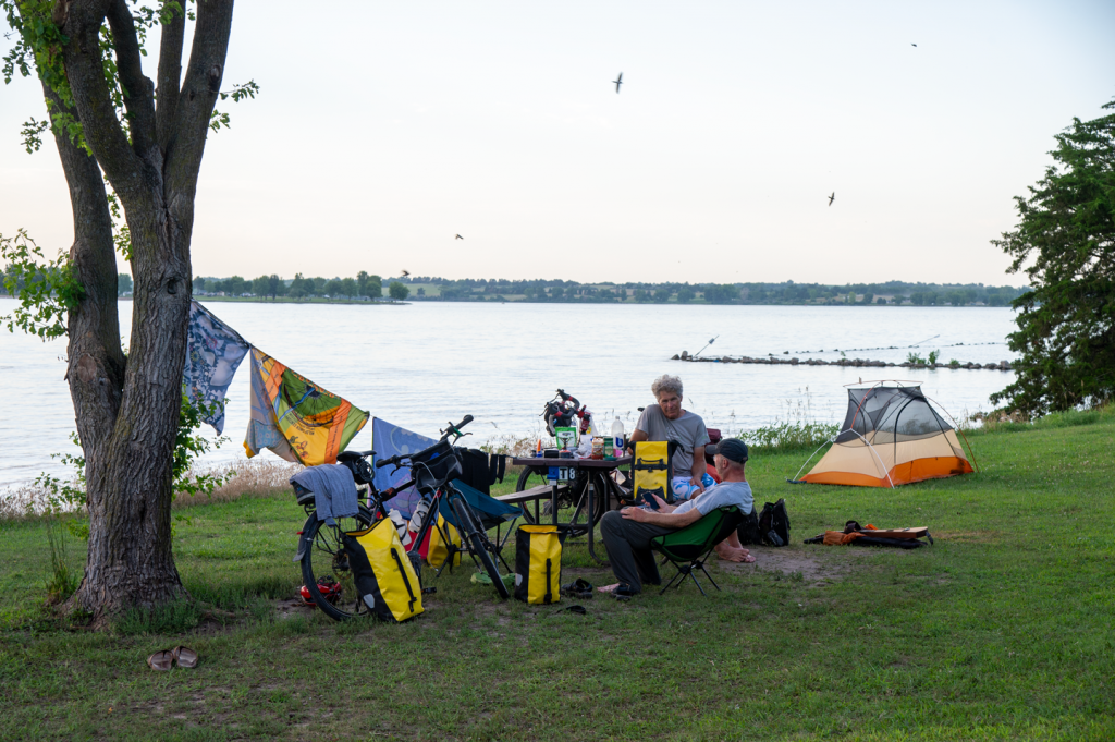 two men relax near a lake their laundry drying at their tent camping site