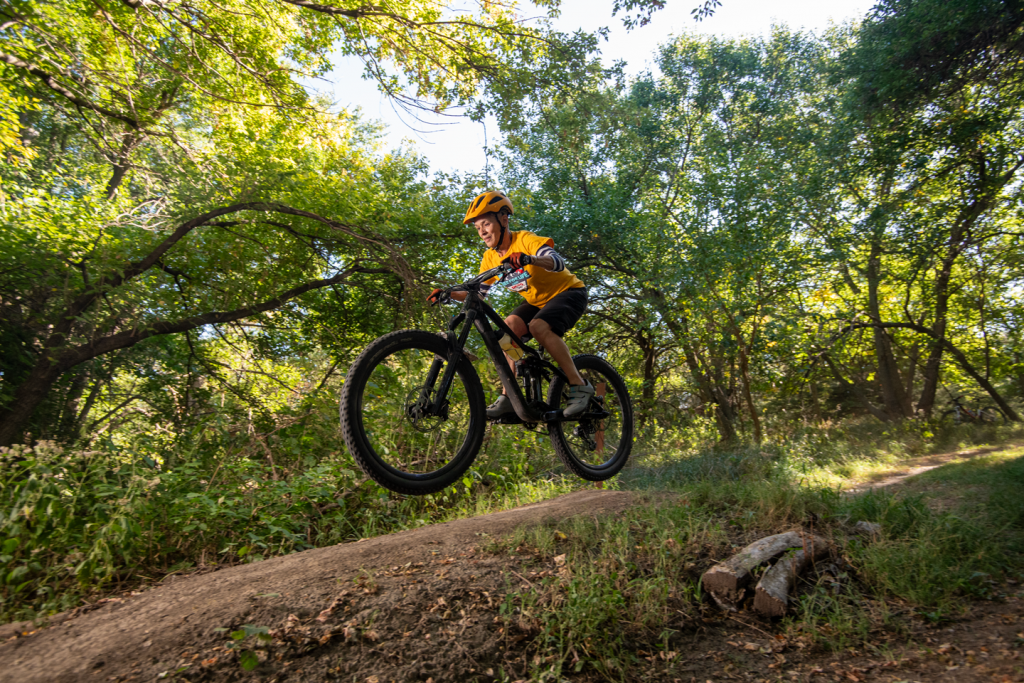 A woman ramps her mountain bike over a dirt hill