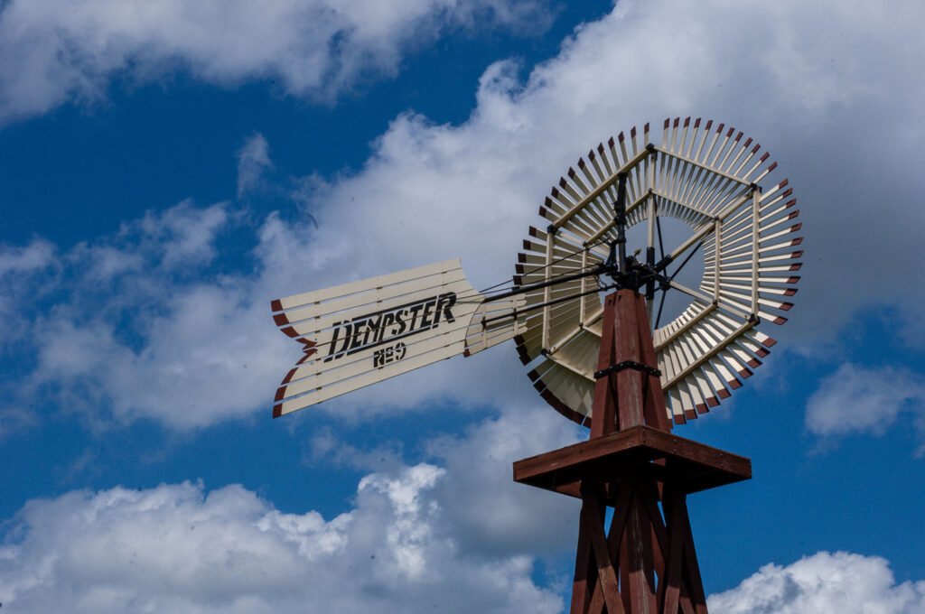 a closeup of an old metal windmill that reads "Dempster" against a blue sky with clouds