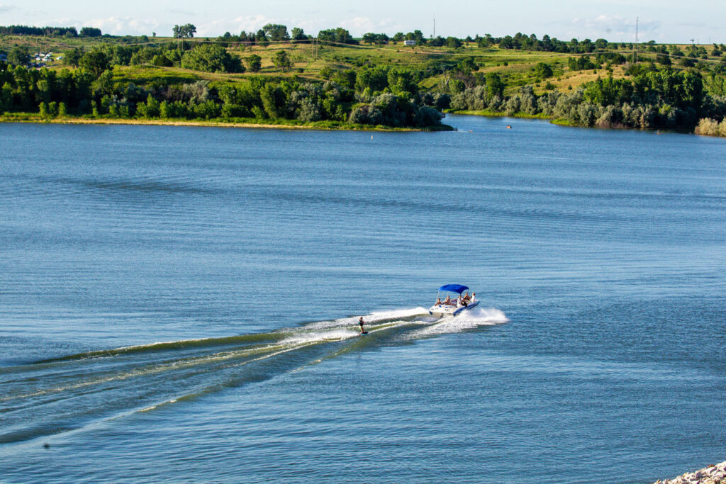 A motorboat pulls a wakeboarder across the blue lake on a sunny day