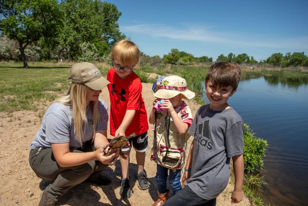 A park staff member holds a painted turtle to show small children at an outdoor wildlife education event in a state park.