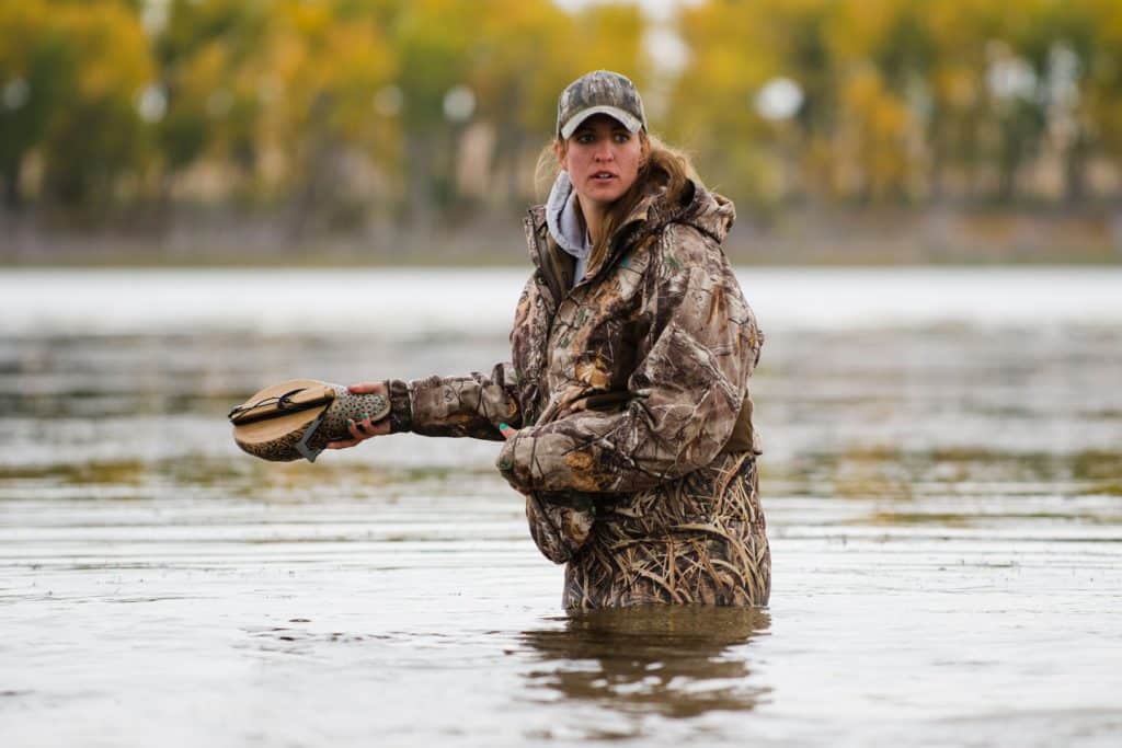 A woman picks up duck decoys in a shallow lake after a day of duck hunting in the fall