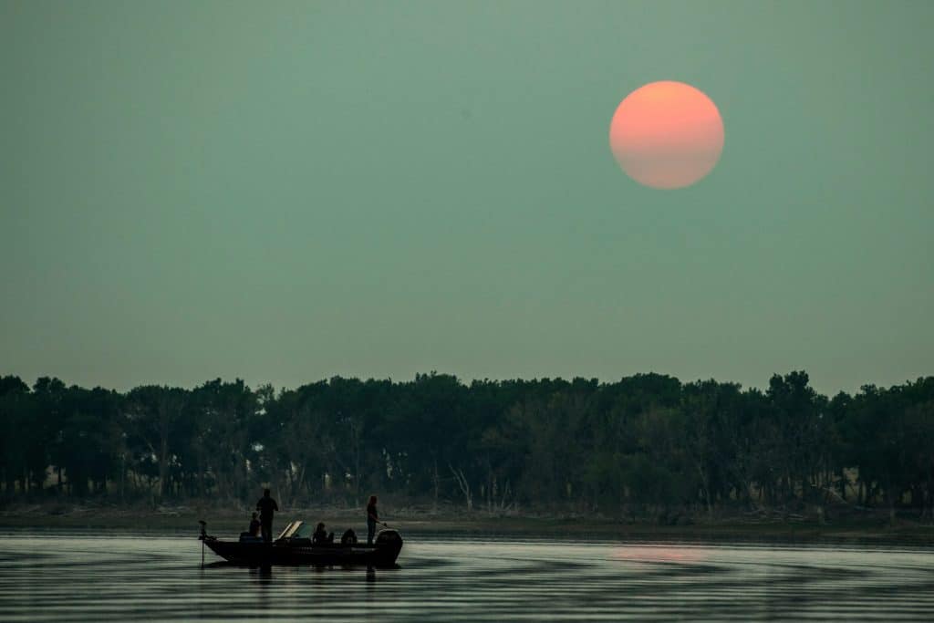 A pink moon hangs over a lake at dusk while anglers fish on a boat 