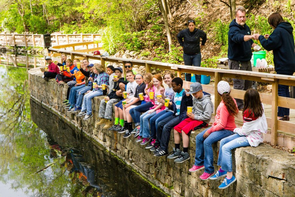 Students sit on bridge anticipating the release of rainbow trout fingerlings.