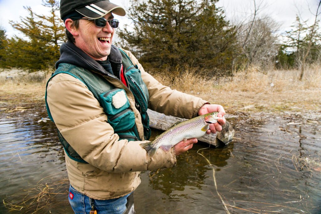 a smiling angler holds a rainbow trout that they caught at the lake