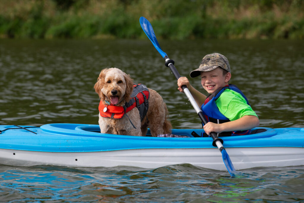 A boy kayaking with this dog on a lake. 