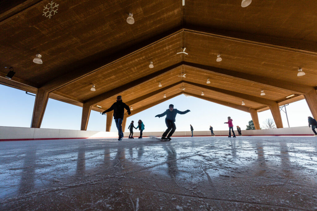 a person at the outdoor ice skating rink skates toward the camera while other skaters are in the background