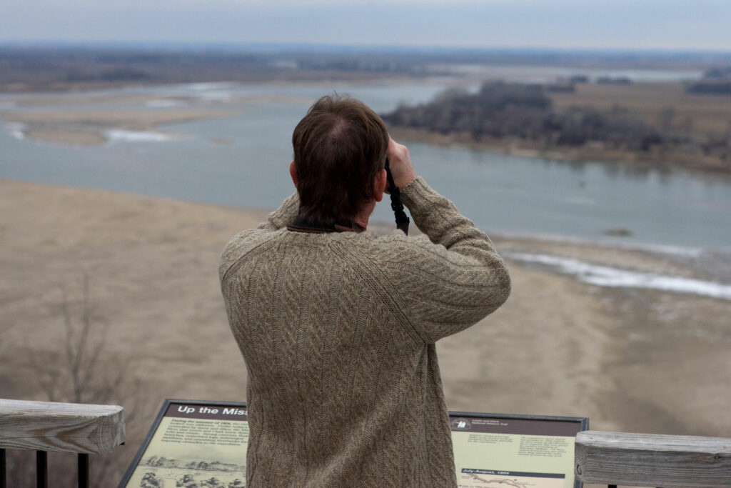 A man uses binoculars to look out over the river where Nebraska, Iowa and South Dakota borders meet.