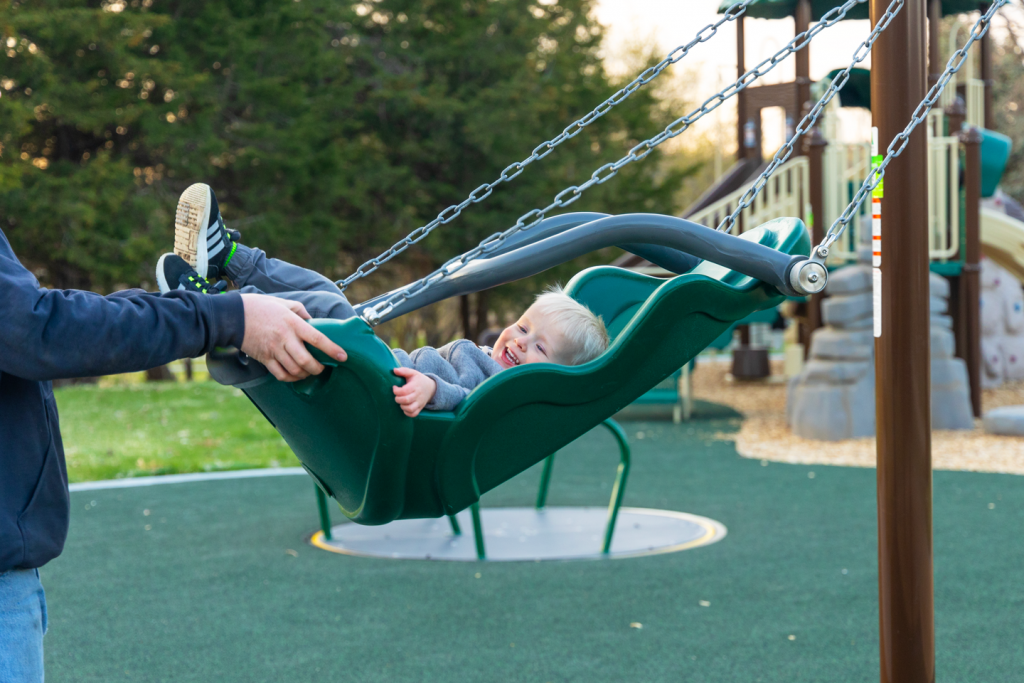 a young boy smiles as he is pushed in a swing