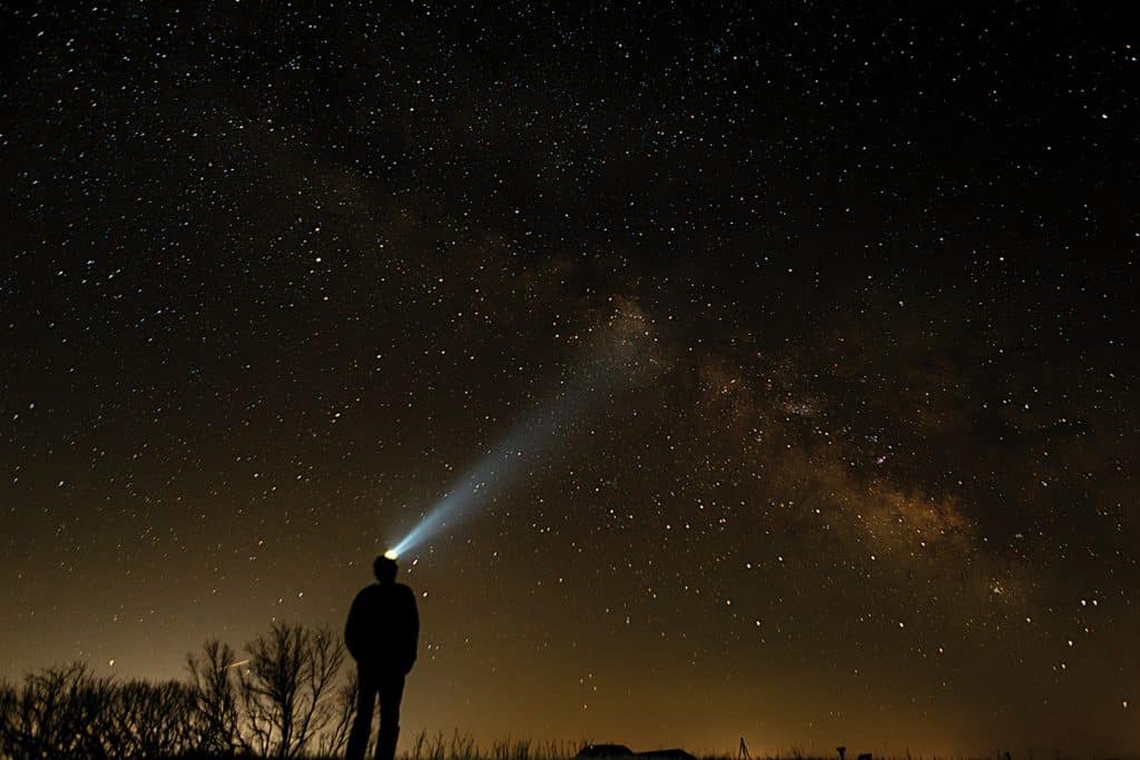 Silhouette of a man wearing a head lamp staring up at the Milky Way at night.
