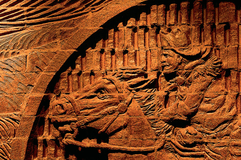 A brick relief sculpture show a racing horse and rider, the wind blowing their hair.