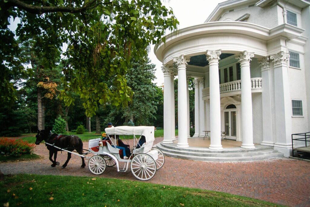A stagecoach pulled by a black horse drives in front of the Arbor Lodge mansion.