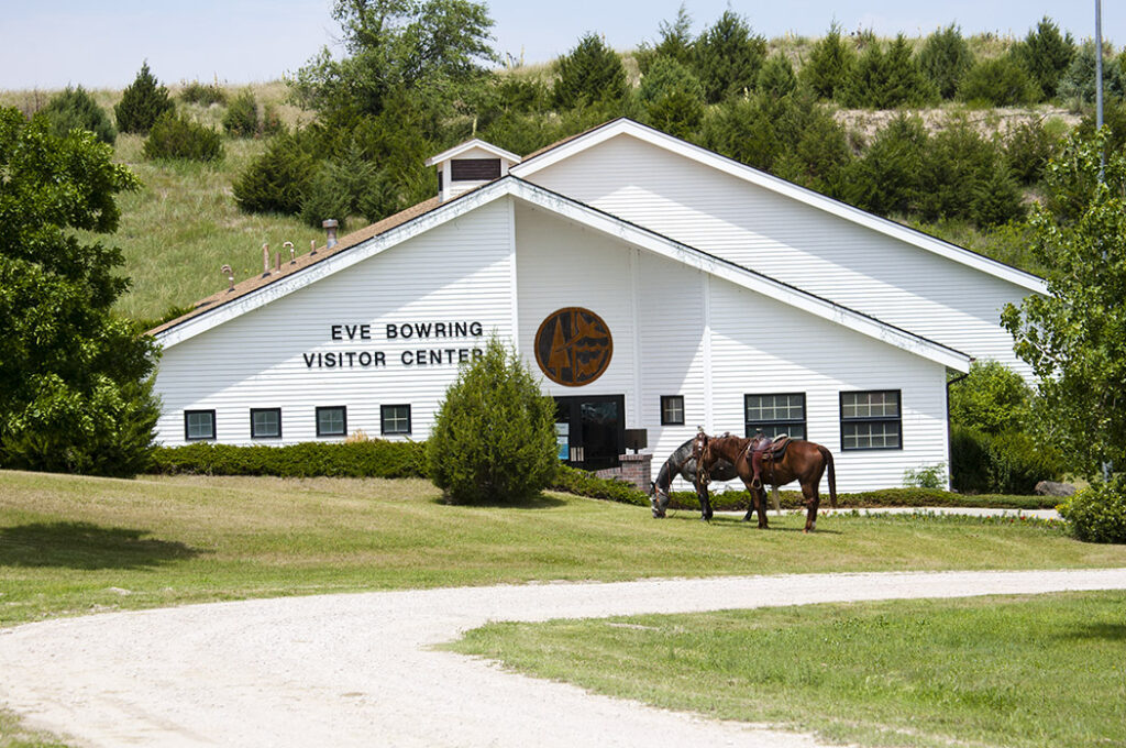 view of a white building that reads "Eve Bowring Visitor Center" with two horses in front of it