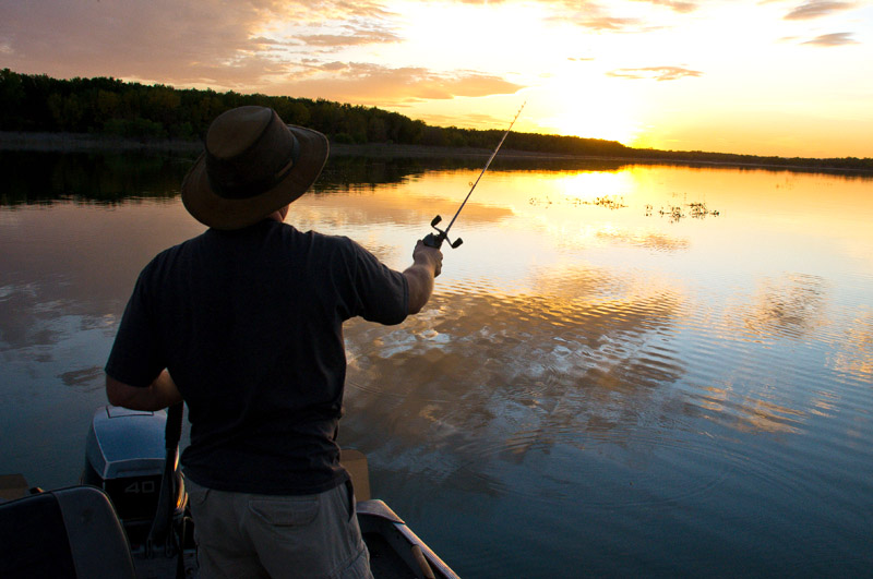 a person fishing from a boat on the lake is silhouetted against the sunset