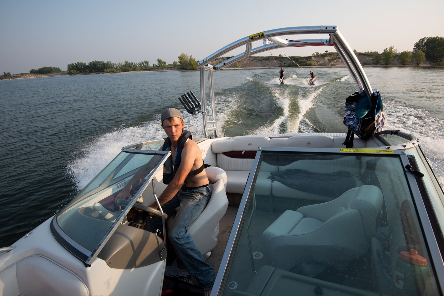 A young man drives a speed boat, pulling teens on wakeboards