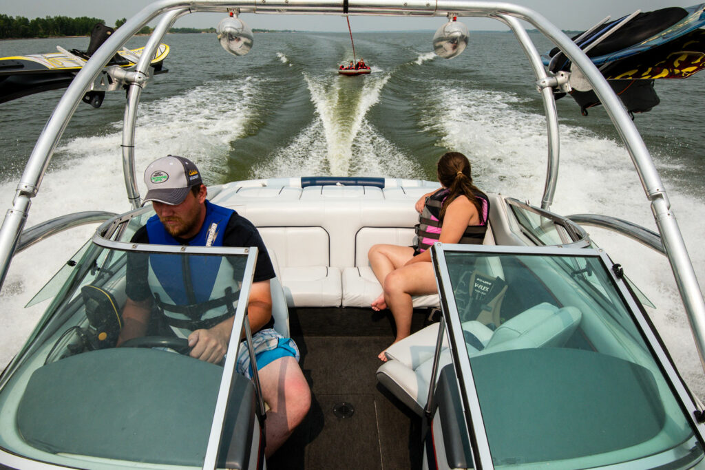 A dad and daughter are in a speed boat pulling a ski tube behind them