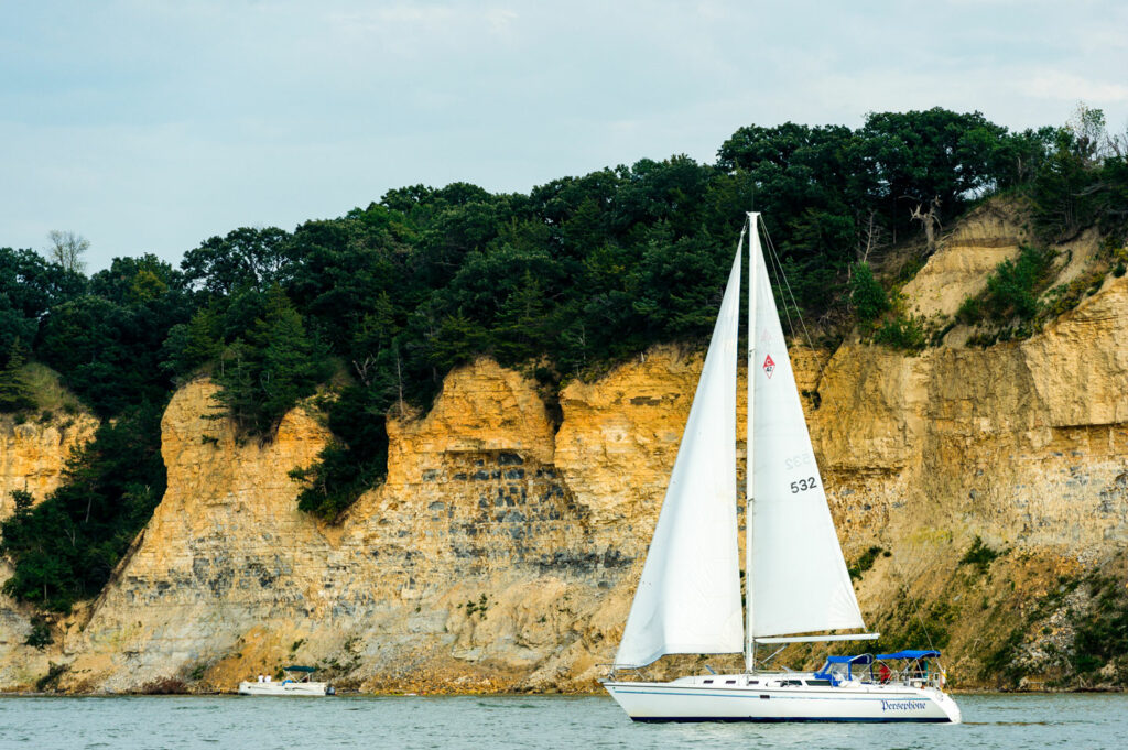A sailboat with white sales passes by a rocky bluff at Lewis and Clark Lake.