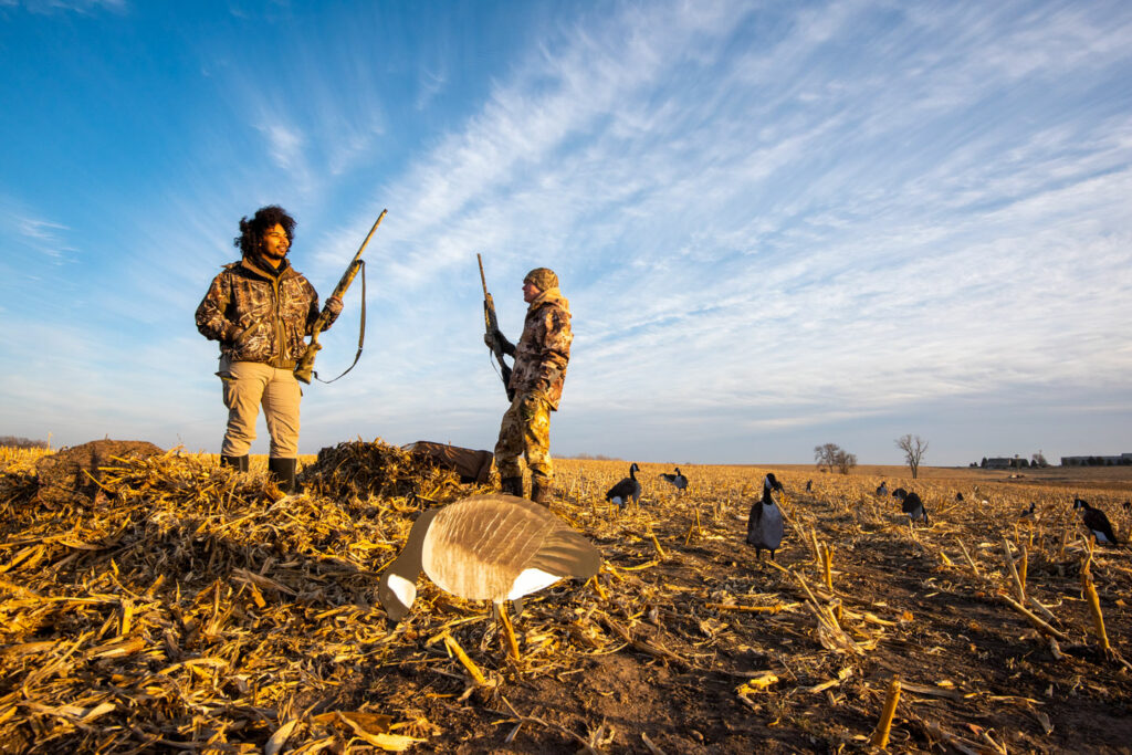 Two young men stand in a corn field hunting for geese.