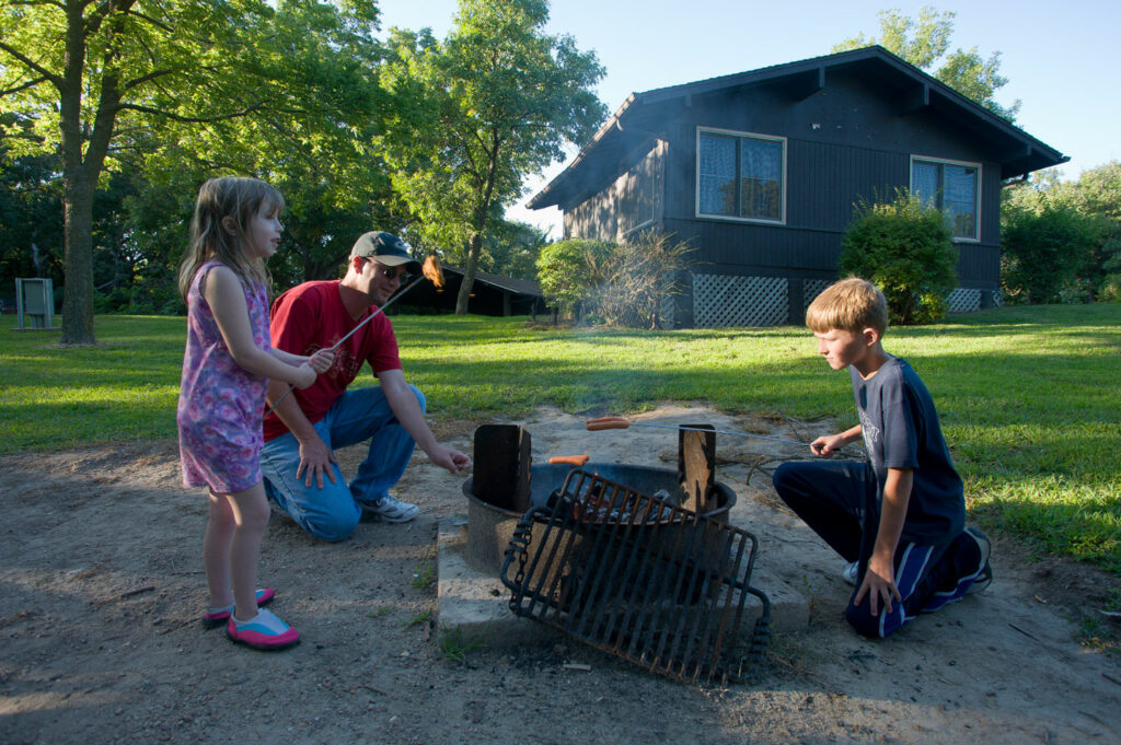 Visitors cooking over campfire near a camper cabin