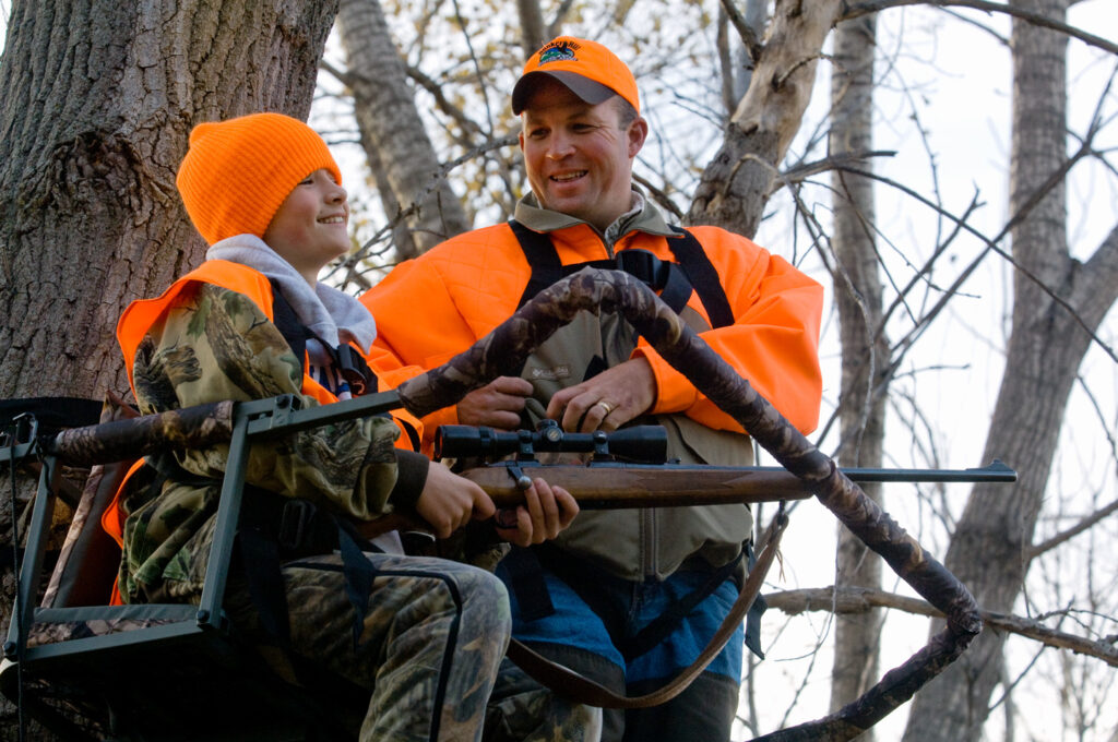 A boy and his dad sit in a tree stand