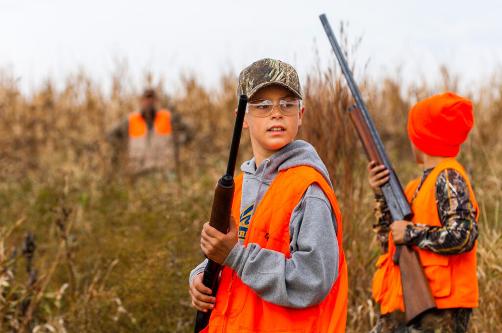 A boy in hunter orange holds his rifle.