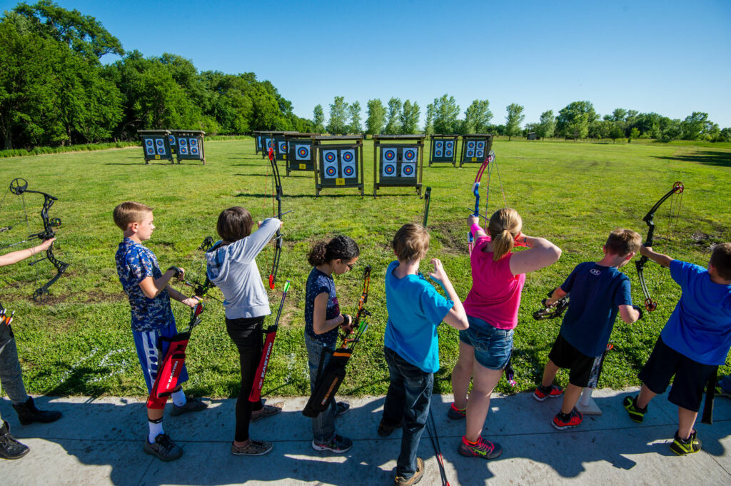 A row of children shoot arrows at a target.