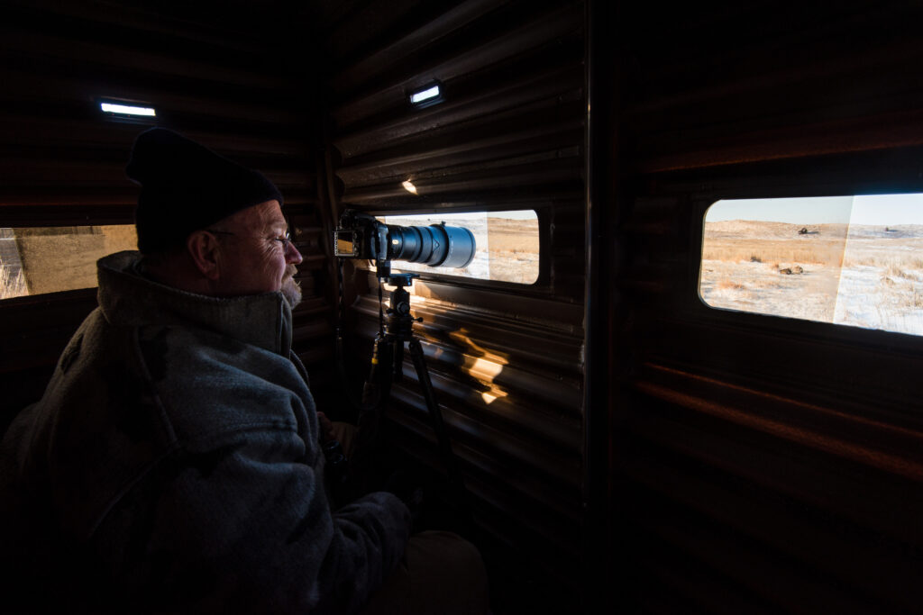 Man taking a picture through a wildlife viewing blind.