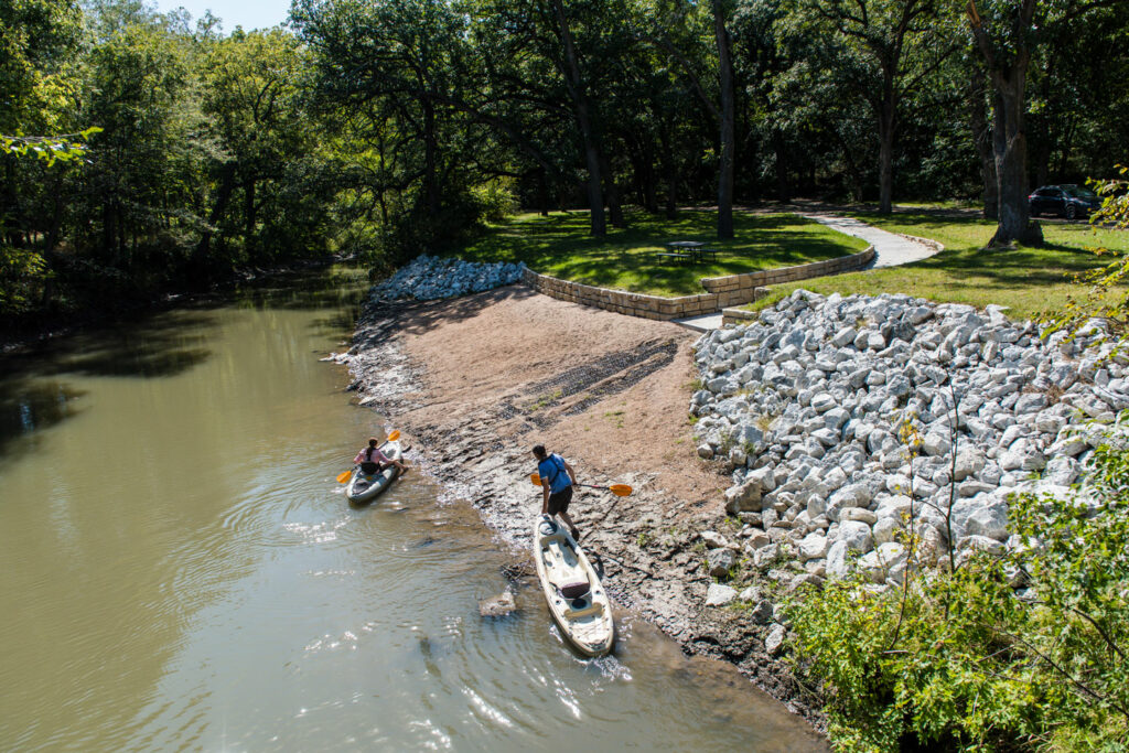 two kayakers prepare their watercraft from a launch point on the river