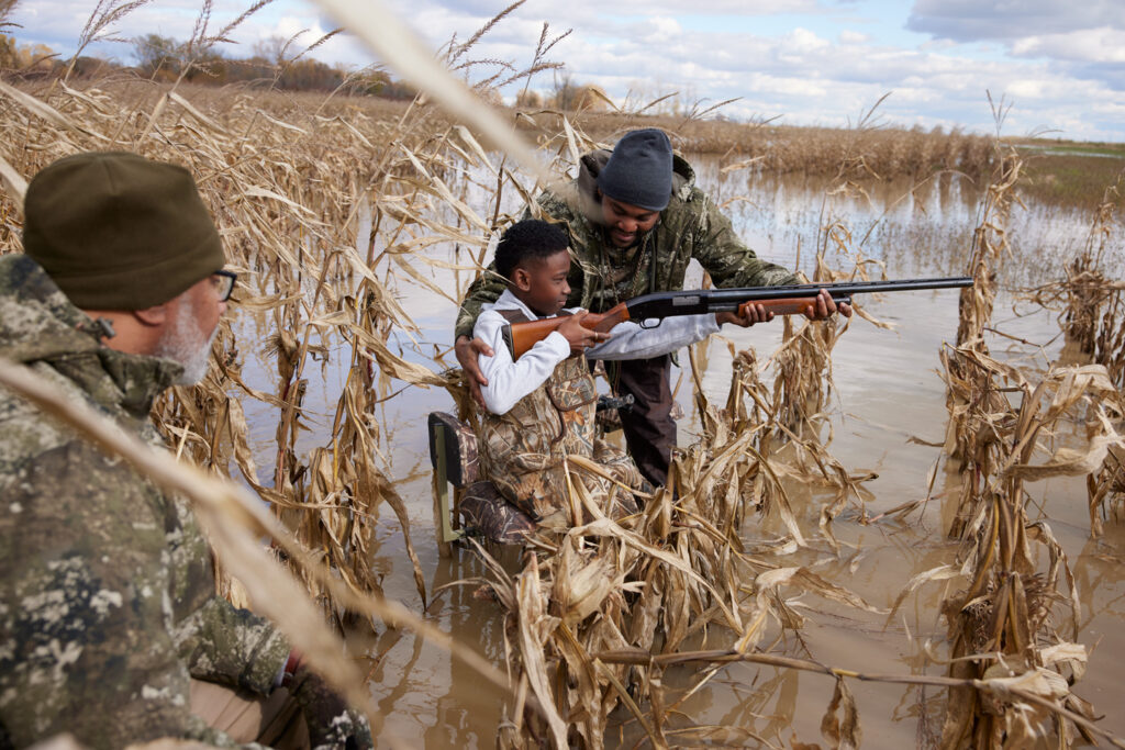 A dad helps his son hold a firearm to shoot ducks