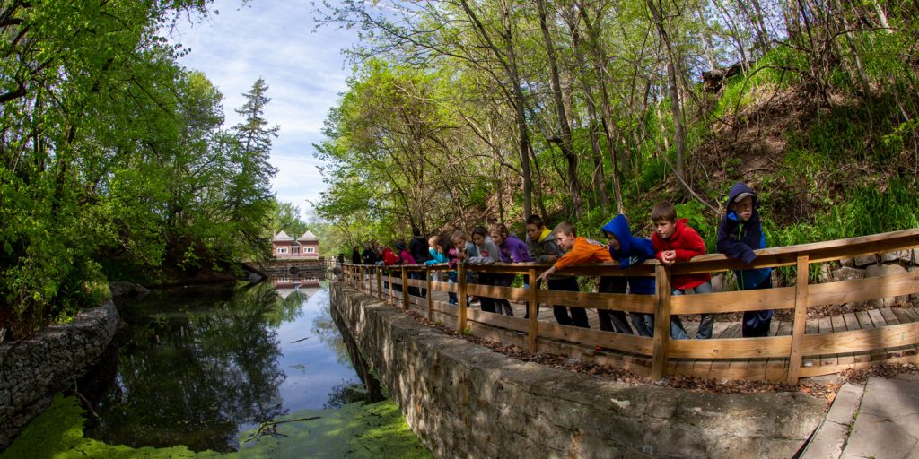 Children stand along a bridge by a pond