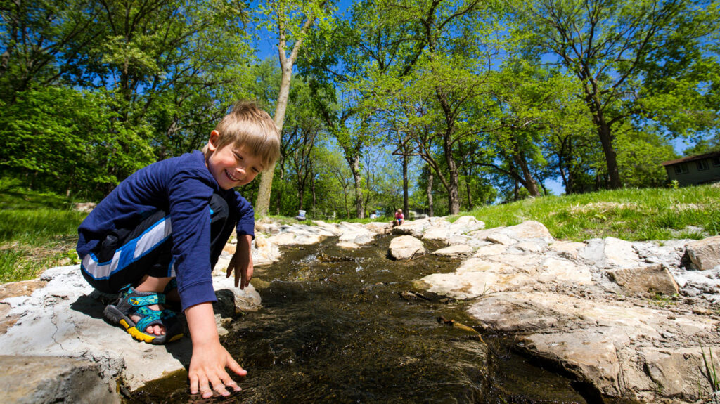 a young smiling boy reaches into the creek