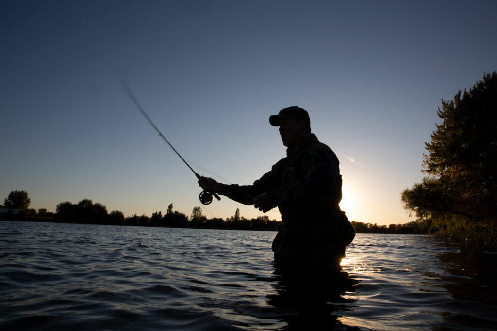 A man fly fishes at dusk while standing waist deep in War Axe lake.