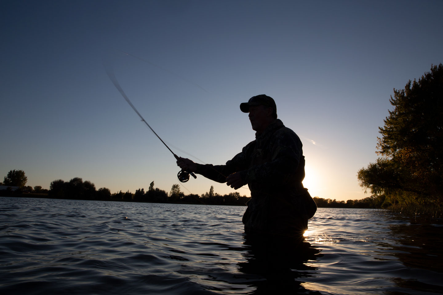 A man fly fishes at dusk while standing waist deep in War Axe lake.