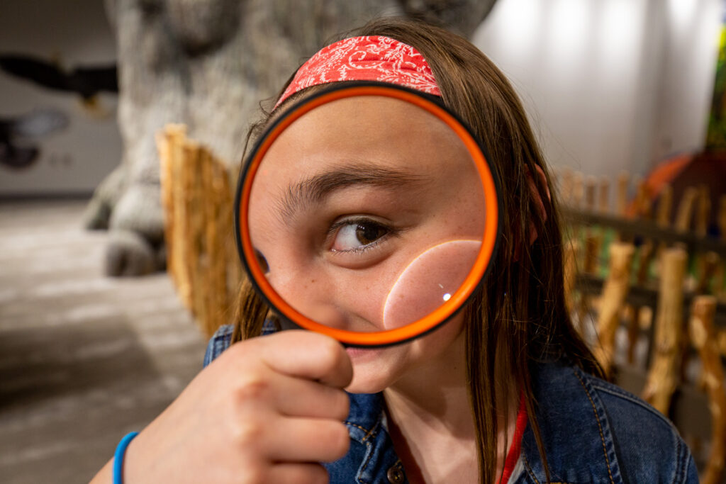 A girl holds an orange magnifying glass up to her eye.