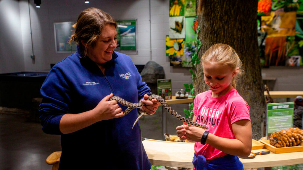 a student smiles while interacting with a snake with the help of a naturalist