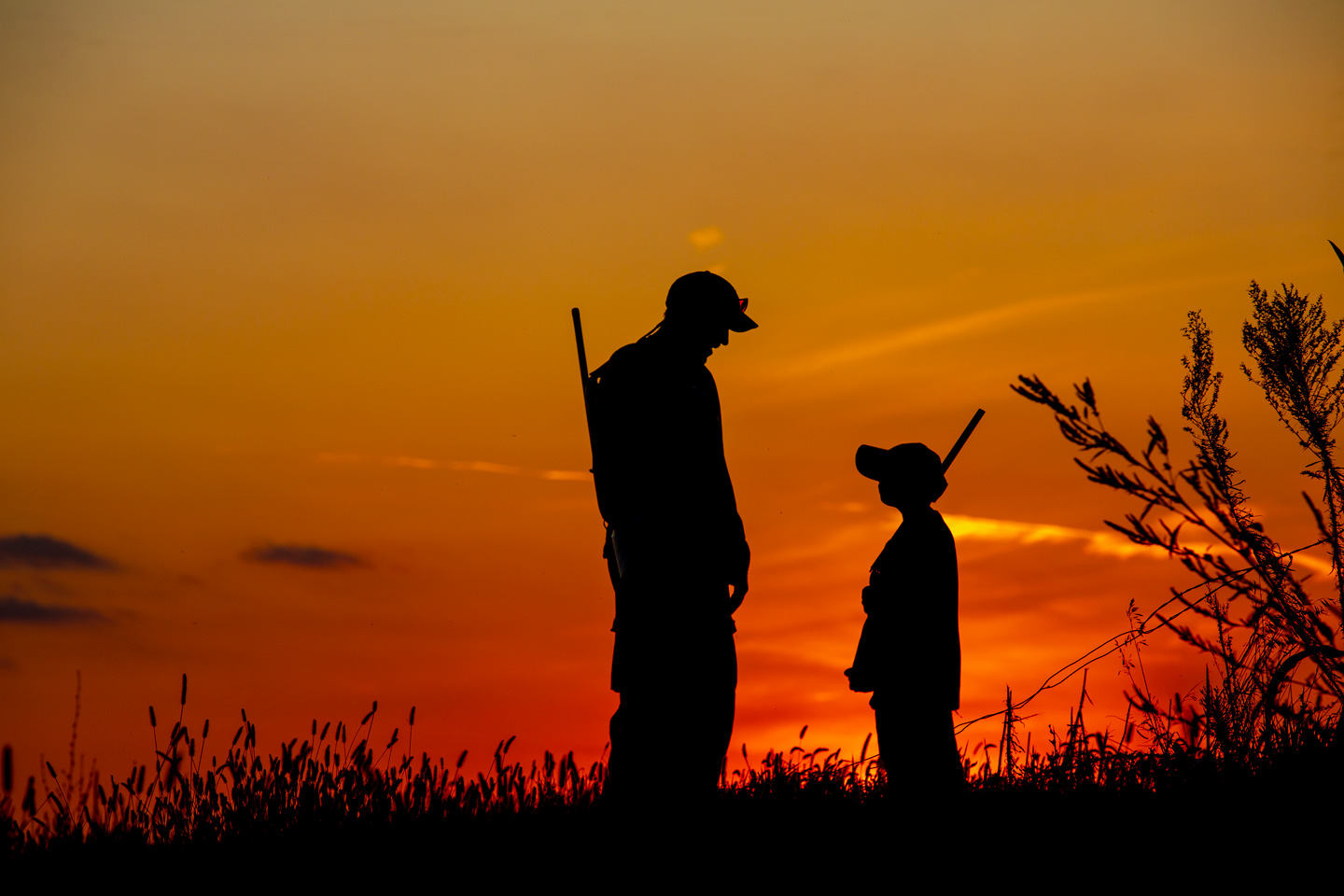 An older man and a small boy are silhouetted by a setting sun