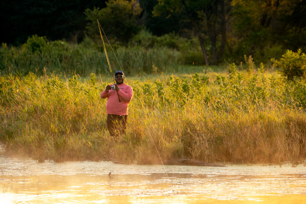 A man fishing from the bank, standing in high vegetation.