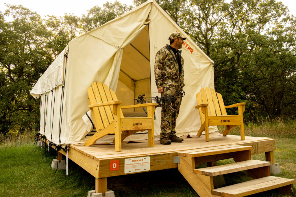 a smiling hunter steps out on the deck of a canvas glamping tent, excited to start his day in the outdoors