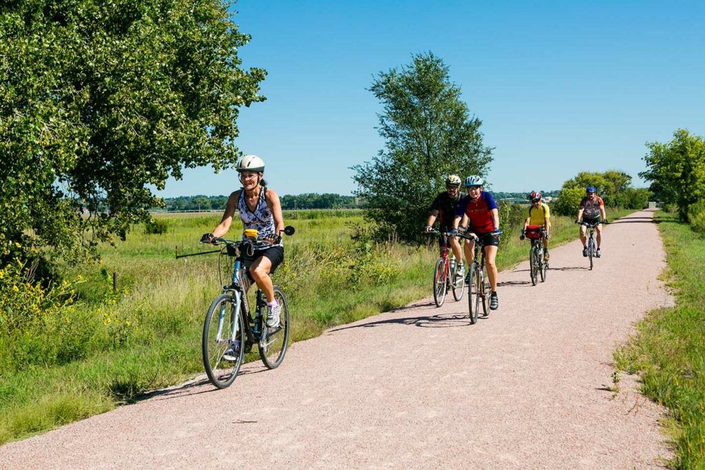 Five smiling bicyclists ride a limestone trail on a sunny day