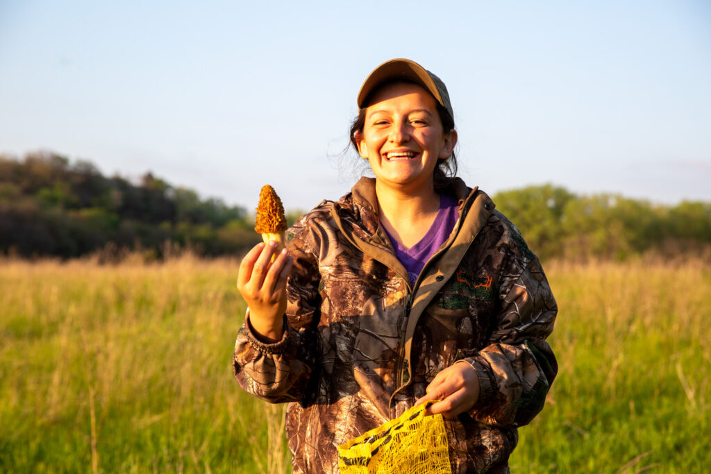 A woman holds up a small morel mushroom