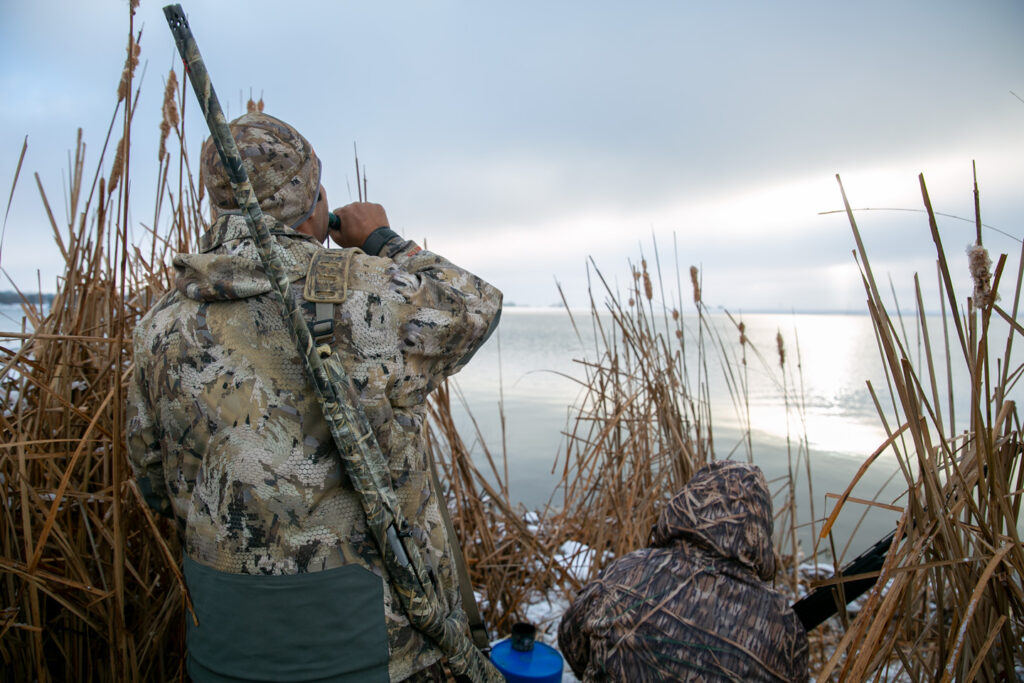 A man facing away from the camera holds a duck call to his mouth.