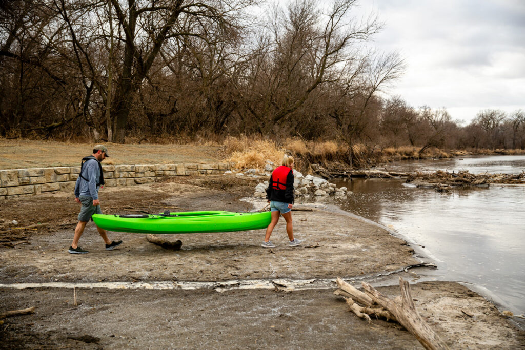 two people carry a kayak to the launch point of the river