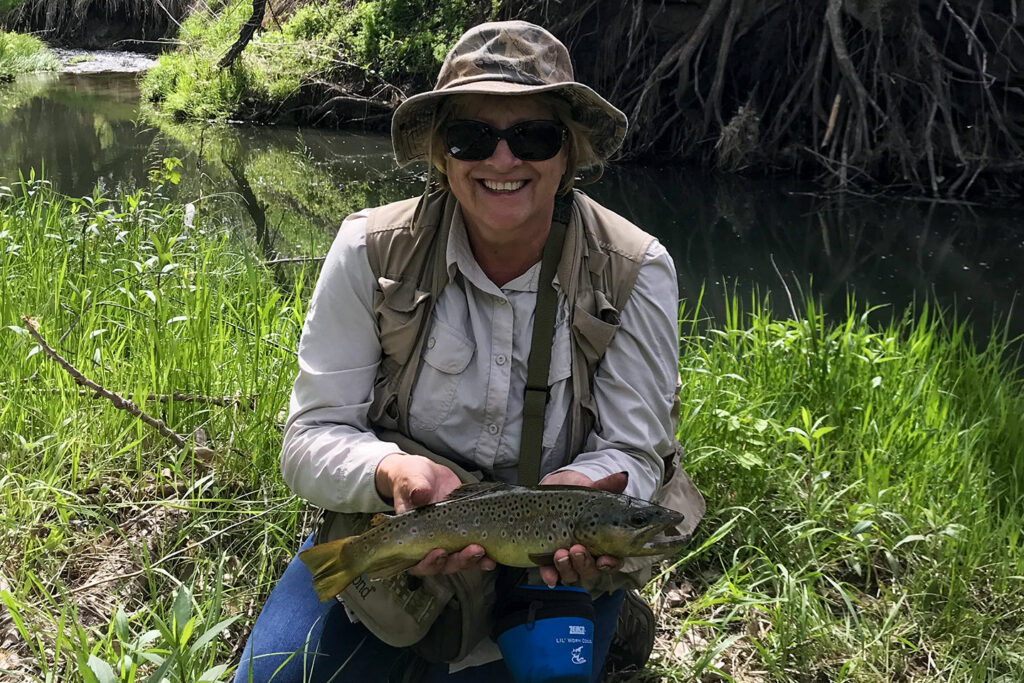 woman holding trout by a stream