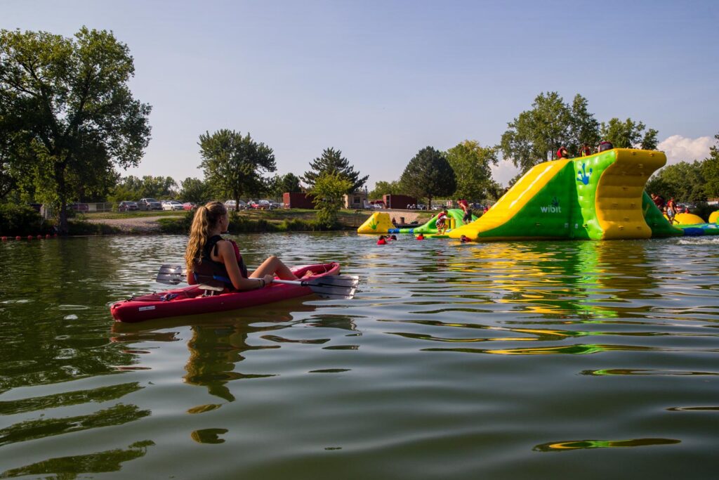 At Louisville State Recreation Area in Cass County, people enjoy the floating playground, while a lifeguard in a kayak is on watch in the foreground. Copyright Nebraskaland Magazine/Nebraska Game and Parks Commission.