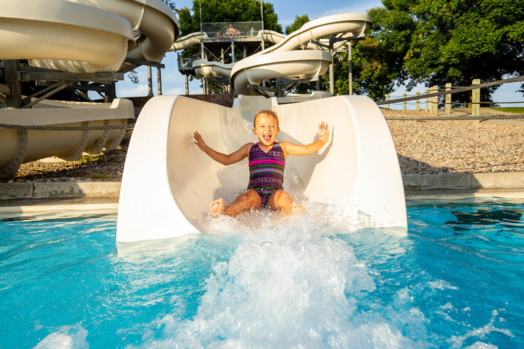 A young girl rides the water slide into the water at the aquatic center pool at Eugene T. Mahoney State Park