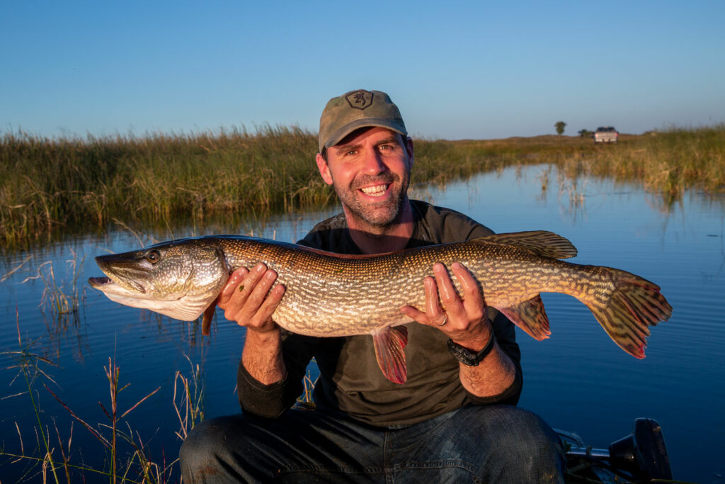A man smiles and holds a master angler-sized northern pike caught at Valentine National Wildlife Refuge in Nebraska